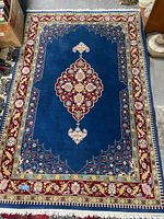 Full view of the Persian Kerman rug showing central medallion and border patterns with blue field