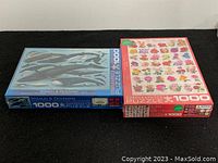 Two boxed Eurographics puzzles side by side on a black surface, one with whales and dolphins, the other with roses.