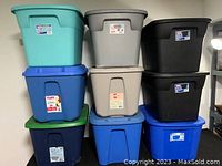 Nine assorted plastic storage containers stacked in three columns, various colors including teal, blue, black, grey, beige and green