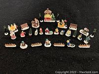 Photo of entire collection of 30 assorted Christmas village figurines and accessories on black cloth, showing variety of figures, benches, lamp posts, fences, trees, and wishing well.