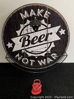 Round wooden hanging sign, dark brown with white text 'MAKE Beer NOT WAR'. Mounted black cast iron bottle opener above a wire basket for bottle caps.