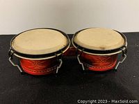 Front diagonal view showing red bongo drums, natural skins, black hardware and design detail.