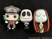 Three Funko Pop vinyl figurines including Beetlejuice with hat that says 'GUIDE', Jack Skellington, and Sally.