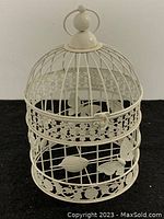 Side view of white painted metal bird cage showing decorative floral and butterfly detail, vertical bars, and rounded dome shape with ring handle at top