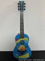 Front view of Minions-themed acoustic guitar showing colorful graphic on body with text "Groovy Day Minion."