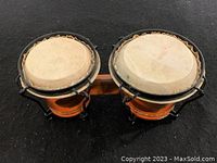 Top angle photo of the pair of small bongo drums showing the natural skin drumheads and black tuning hardware, mounted on a wooden connector bar.