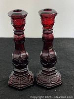 Front view of the pair of ruby red glass candle sticks showing their detailed pressed glass patterning and hexagonal bases.