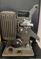 Side view of the Keystone movie projector showing the body, handle, film reel arm, and control knobs.