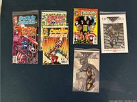 Six comic books including multiple Captain America issues and Fallen Son Wolverine in protective sleeves on a blue surface.