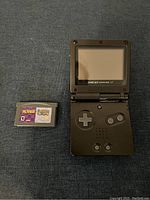 Top view of black Gameboy Advance SP handheld console and Dr. Mario game cartridge side by side on fabric surface.