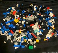 Top view of loose LEGO blocks spread over a surface, showing a variety of bricks, plates, wheels, and printed pieces in multiple colors.