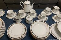 Display of cups and saucers, teapot, sugar bowl, creamer, smaller plates showing floral gold trim design.