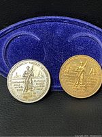 Front side of the two coins showing the seated miner figure and metals listed around the edge, in silver and brass colors respectively.