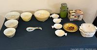 Wide view of mixed bowls, small plates, ice crusher, and Betty Crocker grill on black cloth.