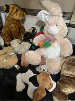 Photo showing a large beige bunny with a carrot and multiple brown and white dog plush toys along with monkey and bear plush.