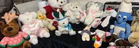 Wide view of the lot showing multiple stuffed animals including Sylvester, white and beige teddy bears, Smurf, and a plush reindeer in a red sweater