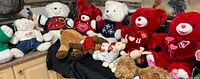 Wide view of multiple stuffed teddy bears and plush toys on black cloth showing variety and details