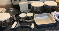 Full display of Pampered Chef lot including non-stick skillet, glass bowls with lids, rectangular baking pan, white dual roller tool.