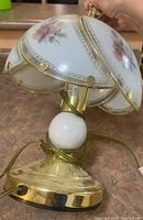 Photo showing lamp tilted on its side to display the glass dome shade with painted pink roses and brass base with white spherical accent.