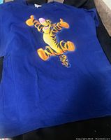 Blue T-shirt with large colorful Tigger graphic print on front side, laid flat on surface.