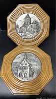 Two octagonal wooden framed pewter relief plaques stacked vertically, showing intricate German town scenes, one with a tower and church, the other with a prominent town hall building.