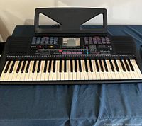 Front view of Yamaha PSR-220 keyboard with attached music book stand on top and placed on metal stand.