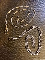 Both watch chains laid flat on a dark surface showing chain styles and clasps.
