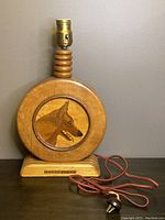 Front view of antique wooden lamp featuring round body with wolf head design and visible electrical cord with fraying.