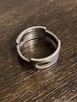 Angled close-up of chunky sterling silver ring showing cut-out teardrop design and open adjustable band on rustic wooden surface.