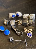 Front angled view of 4 pairs cufflinks arrayed with tie clip and lapel/tie pins arranged on surface