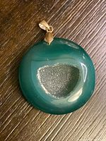 Green agate geode pendant showing overall polished smooth surface and rounded shape with metal bail on top.