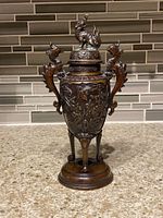 Front view of Japanese bronze incense burner showing floral design, handles, and animal finial on the lid.