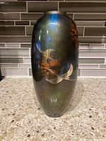 Oblique front view showing the vase's smooth metallic glaze with stylized bird decoration.