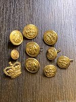 Top side view showing 9 round gold-tone military pins with crown and anchor emblem, and 1 crown-shaped pin for size and detail.