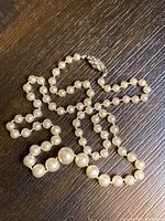 Full view of the 18-inch faux pearl strand necklace laid on a dark wooden surface showing the graduated pearl sizes and clasp.