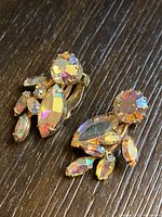 Close-up image of one earring showing round and marquise-shaped iridescent rhinestones set in gold-tone clip-on backing.