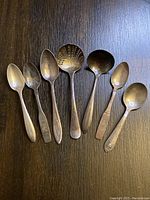 Seven varying spoons laid out on a dark wooden surface showing size and shape differences.