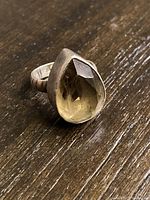 Close-up photo of sterling silver ring with pear-shaped yellowish faceted gemstone on wooden surface.