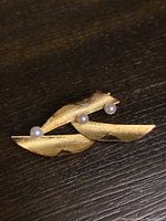 Front view of the gold vermeil brooch pin with three pearls on wooden surface.