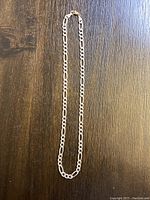 Full length view of the Italian Figaro chain necklace laid flat on a wooden surface showing copper clasp.