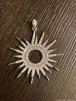 Front view of the sunburst shaped sterling silver pendant with rhinestones set in the middle circle and some rays.