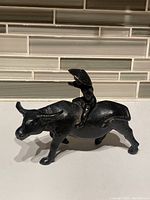 Bronze sculpture front and side views showing child figure on back of water buffalo with dark patina and worn surface.