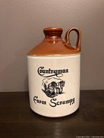 Front view of a brown and cream stoneware jug with a handle and printed design of horses and text 'Countryman Farm Scrumpy'.
