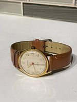 Gold-tone Westclox automatic wristwatch with white dial and brown leather strap shown from side angle in daylight. Dial shows some scratches.