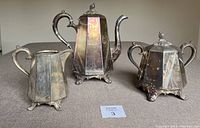 Full view of the three-piece antique silver tea set showing teapot, sugar bowl, and cream jug on a flat surface.