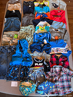 Photo of multiple baby and toddler clothing items arranged on a surface including pants, shirts, jackets, swim shirts.