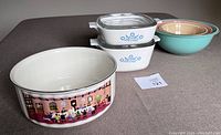 Image shows a Villeroy & Boch round baking dish with colorful kitchen scene, three pastel colors Pyrex mixing bowls, and two Pyrex rectangular dishes with lids.