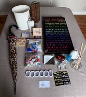 Photo showing all items in the lot arranged on a surface, including white wastebasket, soap dispenser, inspirational prints, sewing accessories, umbrella, diffuser reeds, clips, and decorative items