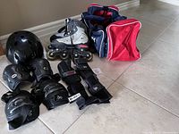 Photo showing in-line skates, helmet, wrist, elbow, and knee pads along with red and blue carrying bag on floor.