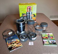 Complete Nutribullet blender set displayed on a table showing blender base, cups, lids, blades, and two recipe books along with the product box.